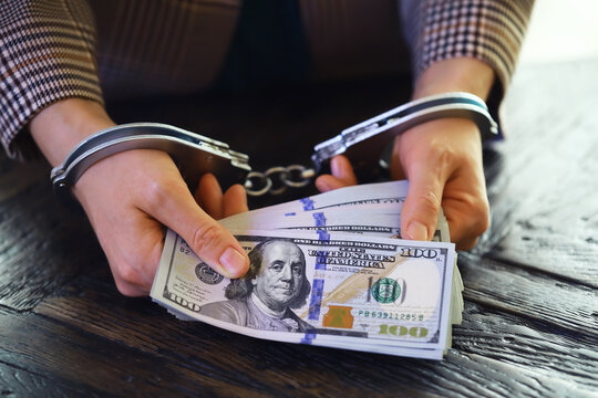 women's handcuffed hands hold dollars on a dark wooden background