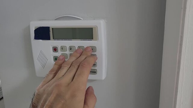 Video footage of a person entering a security code on a wall mounted home alarm keypad. Close up view of a residential security system used for access control, authentication and home protection.