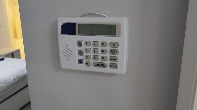 Close up video clip of a hand pressing function buttons on a residential alarm keypad mounted indoors. Home security system operation, electronic access management and property protection concept.