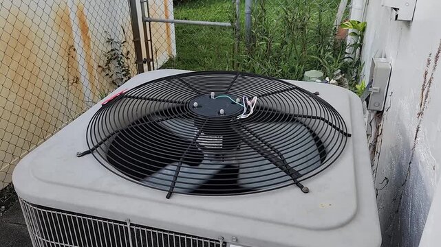 Residential HVAC condenser unit with spinning fan installed outside a building. Climate control equipment providing cooling and air circulation for a home.