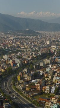 9:16 portrait drone shot of Kathmandu Nepal featuring busy urban cityscape roads and distant snow capped Himalayan mountains under clear daylight