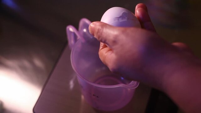 pair of hands cracking an egg to a measuring cup.