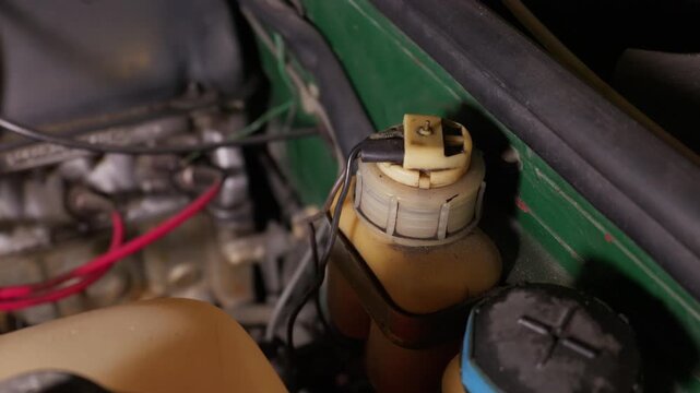Close-up view reveals a brake fluid reservoir with electrical wires inside a green car engine bay. Concept of automotive maintenance, vehicle repair, and vintage car restoration projects.