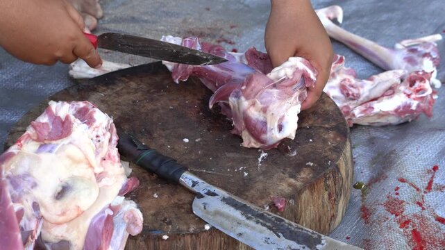 Butcher cutting raw meat on a wooden chopping block