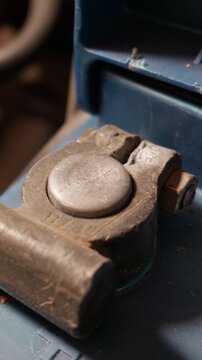 A dusty metal car battery terminal clamps securely onto a lead post against a blue casing. Concept of automotive maintenance, mechanical repair, and electrical power connectivity.