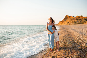 Happy woman with child girl daughter 5-6 year old holding hands walking at beach over sea at...