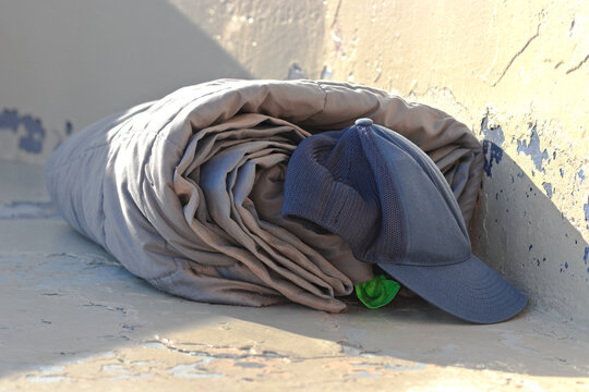 Rolled bedding and a cap sit in a worn urban corner, suggesting homelessness in Long Beach.