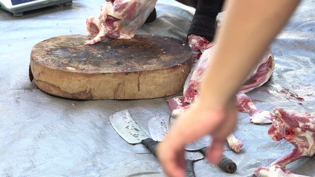 Butcher cutting raw meat on a wooden chopping block outdoors