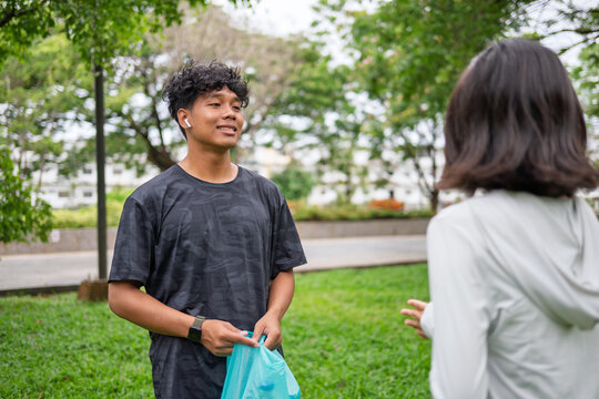 Multicultural Gen Z friends Asian woman and African American mixed race man plogging and collecting trash in green urban park for representing sustainability wellness and positive active lifestyle.