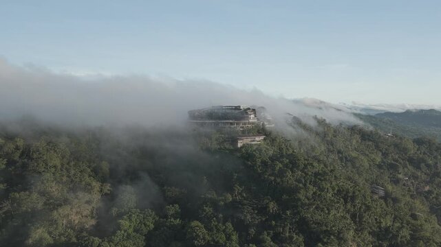 Aerial view of a large building on a lush hillside shrouded in thick fog in Cebu City, Central Visayas, Philippines.