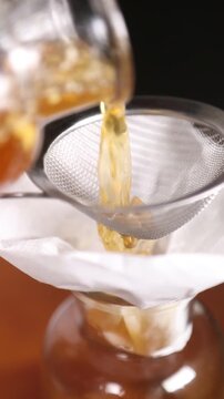 Chef filtrando l&iacute;quido infusionado en c&aacute;mara lenta (primer plano). Un chef profesional colando l&iacute;quido infusionado en c&aacute;mara lenta. Proceso culinario cinematogr&aacute;fico, gastronom&iacute;a moderna.