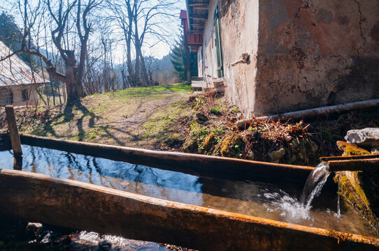 View of the historic Prasnica charcoal burners' settlement with a wooden water trough and rustic stone buildings under a clear sky in Stare Hory, Banskobystricky kraj, Slovakia.