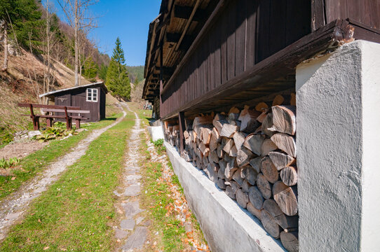 View of Prasnica old charcoal burners settlement with stacked firewood under a wooden porch and a grassy path in Stare Hory, Banskobystricky kraj, Slovakia.