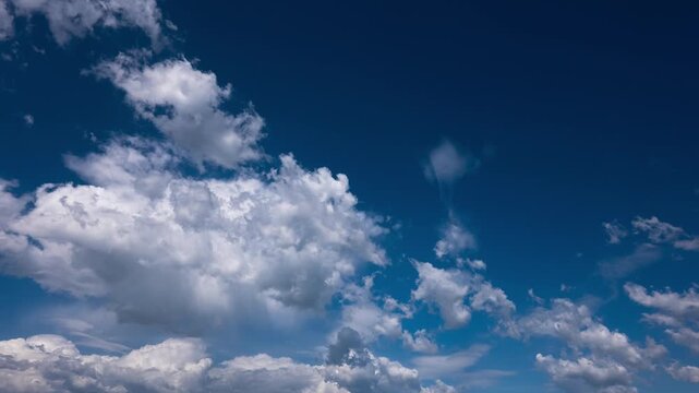 Fluffy white cumulus clouds billow and drift quickly across a vibrant deep blue sky. The accelerated time-lapse captures the dynamic movement of the atmosphere on a bright sunny day.