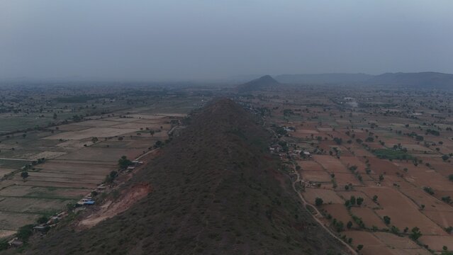 View of a long rocky ridge from above stretching across agricultural fields and rural settlements under a hazy sky in Naugaon, Rajasthan, India.