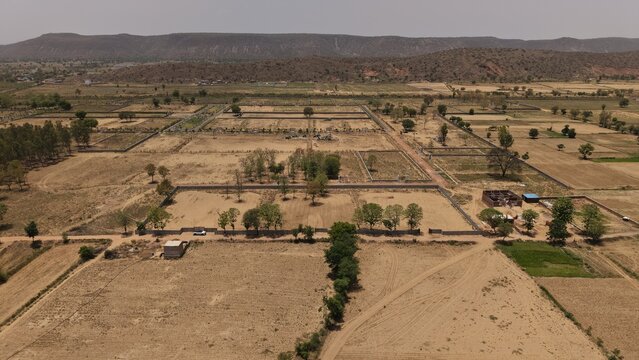 View of the arid landscape with fenced land plots and sparse trees against a backdrop of rolling hills in Naugaon, Rajasthan, India.