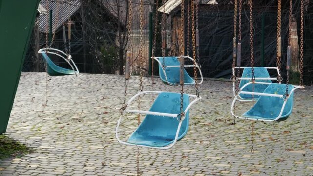 Empty blue swing ride chairs hang from rusty chains in an abandoned amusement park evoking loneliness and abandonment on an overcast day. This visual narrative of decay and lost joy