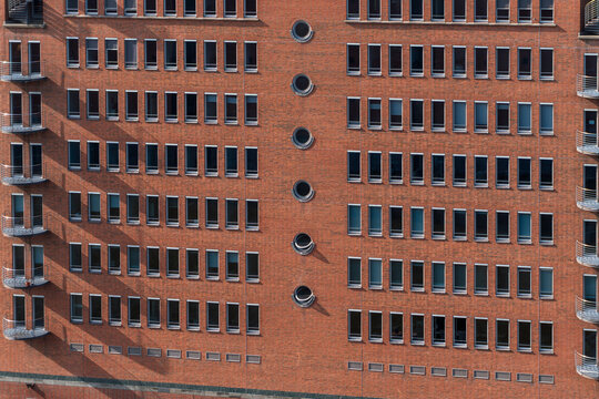 Symmetrical facade of a modern red brick apartment building with rows of windows, balconies, and circular architectural details creating an urban geometric background texture.