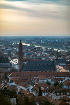 View of the Church of the Holy Spirit and the historic red-tiled rooftops of the old town with the Neckar river in the distance at dusk in Heidelberg, Baden-Wurttemberg, Germany.