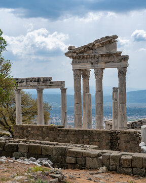 Temple of Trajan ruins, Pergamon Acropolis, Bergama, Turkey. Ancient marble columns stand against a dramatic cloudy sky, overlooking the valley