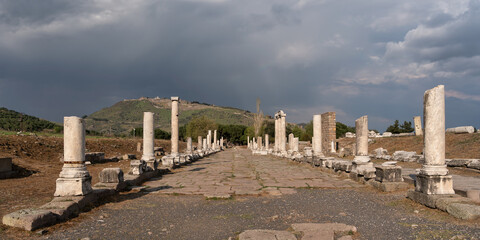 Naklejka premium Sacred Way ruins at Asklepion, Pergamon, Bergama, Turkey. Ancient columns line a stone path leading to distant ruins under a blue sky