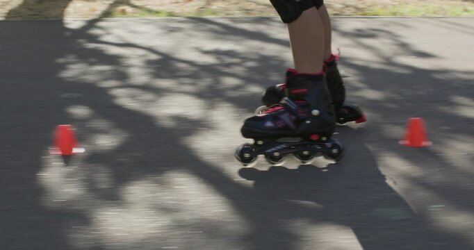 Girl maneuvers around small cones on rollerblades during active park exercise. Child shifts weight turning inline skates to pass marker with controlled movement