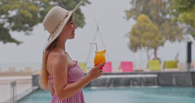 Woman in straw hat smiling and holding tropical orange cocktail, poolside at luxury beach club with outdoor lounge chairs, summer vacation travel and hospitality background