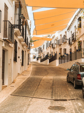 View of a narrow cobblestone street lined with white-washed houses and yellow sunshades in Zuheros, Andalusia, Spain.