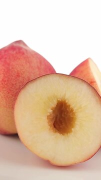 Slowly rotating halved fresh chinese peach on a plate with a white background.