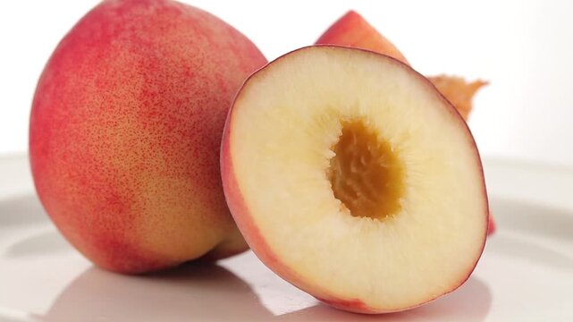Slowly rotating halved fresh chinese peach on a plate with a white background.
