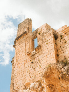 View of the ancient stone walls and ruins of Zuheros Castle built on a rocky cliff under a blue sky in Zuheros, Andalusia, Spain.