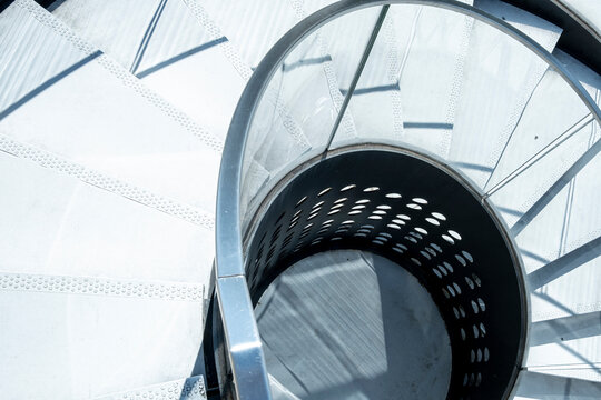 Spiral metal staircase turns through a bright interior, where railings and light trace architecture geometry around a curve structure