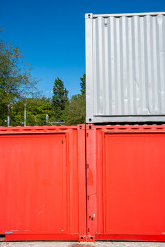 Red containers form an industrial storage yard beneath a white metal structure, with blue sky sharpening the architecture of stacked volumes