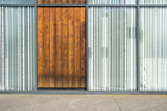 Wood door anchors a metal and glass facade, turning industrial entrance panels into a precise architecture texture across the street front