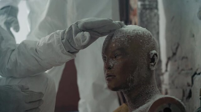 Frost covered mannequin head in derelict laboratory, conservator in protective suit gently touches crystalline residue on scalp while checking sealed sample vial, cracked plaster walls and dusty