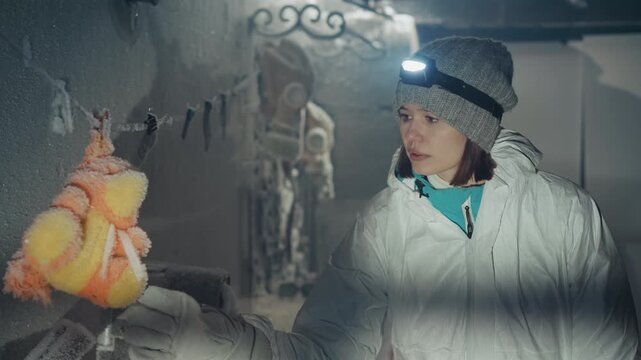 Explorer with headlamp surveys frozen lab, suspended teddy covered in ice crystals, nuclearera equipment and rusted machines in background, cautious hands collect sample, corridor lined with frost