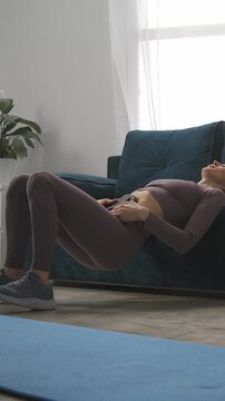 A woman performing a bridge exercise at home in her living room, demonstrating strength and fitness during a home workout routine on a yoga mat with a comfortable couch in the background
