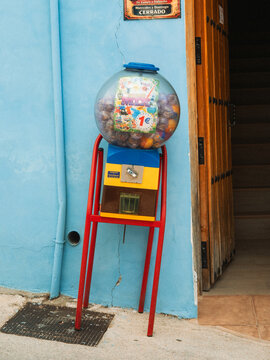 View of a colorful toy vending machine standing against a bright blue wall next to a wooden doorway in Juzcar, Andalusia, Spain.