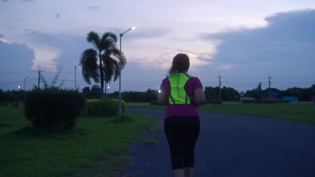 Middle-aged Asian woman jogging safely at twilight with reflective gear and LED arm light