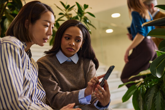 Diverse women colleagues collaborating discussing content on smartphone