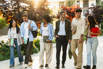 Group of happy students walking together with University professor on college campus, chatting and...