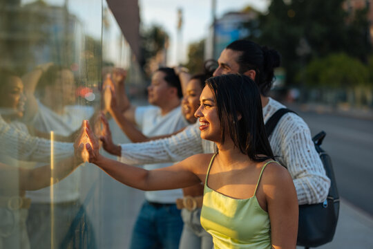 Diverse friends touching urban storefront glass on sunny day