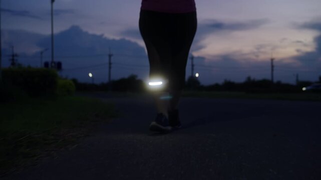 Low-angle front view of a middle-aged Asian woman jogging at twilight with LED safety light