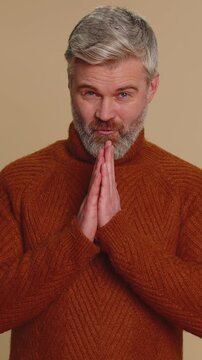 Sneaky cunning middle-aged man with tricky face gesticulating and scheming evil plan, thinking over devious villain idea, cheats, revenge, jokes, pranks. Senior guy isolated on beige studio background