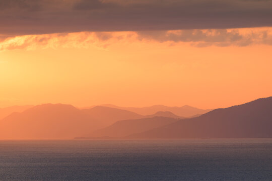 View of silhouetted mountain of the Izu Peninsula ranges across the sea under a vibrant orange sunset sky in Shizuoka, Shizuoka, Japan.