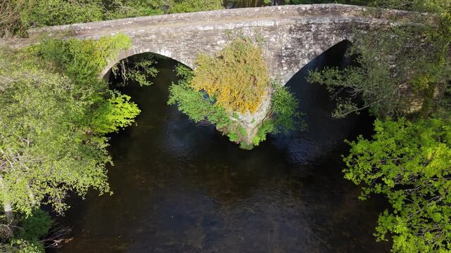 Ancient Stone Bridge Spans The Parga River Near The Capela de San Alberte In Guitiriz, Galicia, Spain. Aerial Pullback Shot