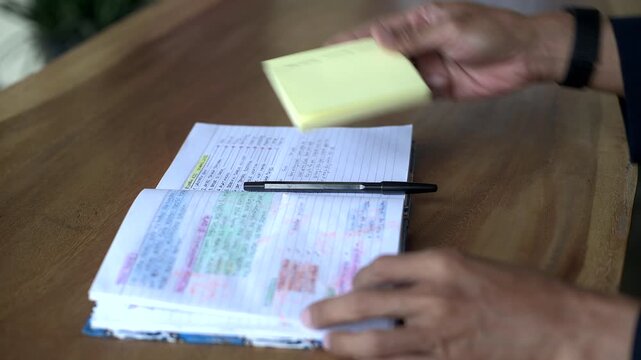 Asian business man open book and placed a pile of yellow sticky notes on top. Close up filmed from still or static tripod