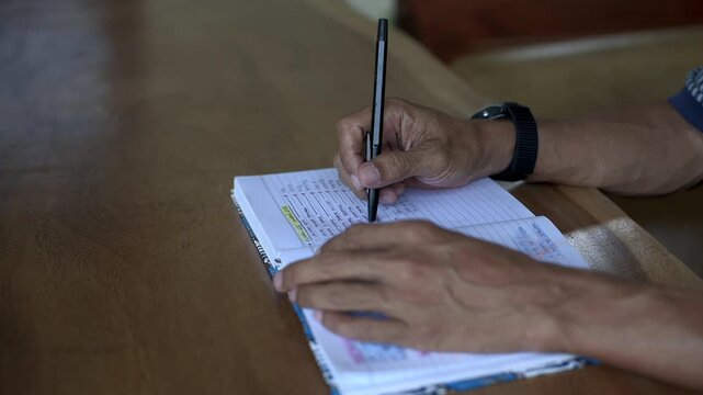 Asian male take a break before continue writing a book while play turning a pen by finger close up static tripod shot