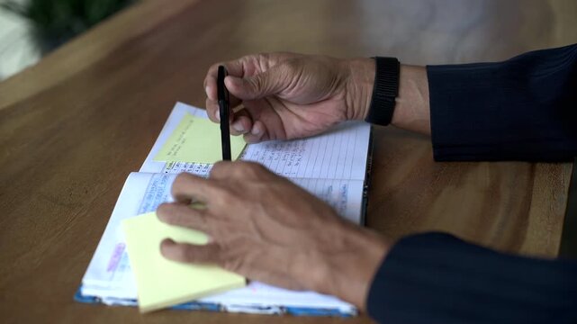 Asian business man sticking yellow note paper on book page. Close up filmed from still or static tripod