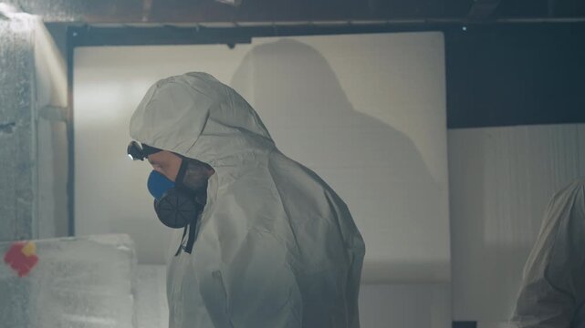 Scientist in hazmat suit inspecting frozen sample inside abandoned house, headlamp beam cutting through frost, gas mask visible, stacked insulated containers, sterile boxes, tense clinical atmosphere